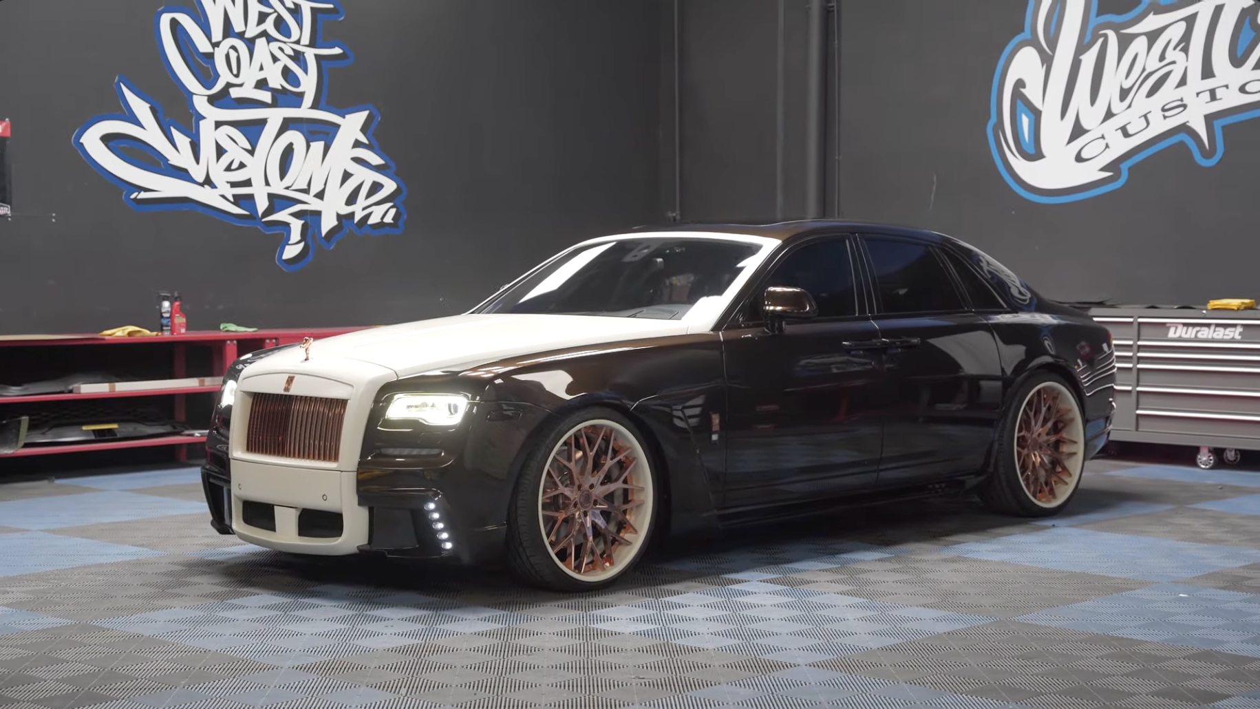 Black luxury car in a garage with 'West Coast Customs' branding in the background.