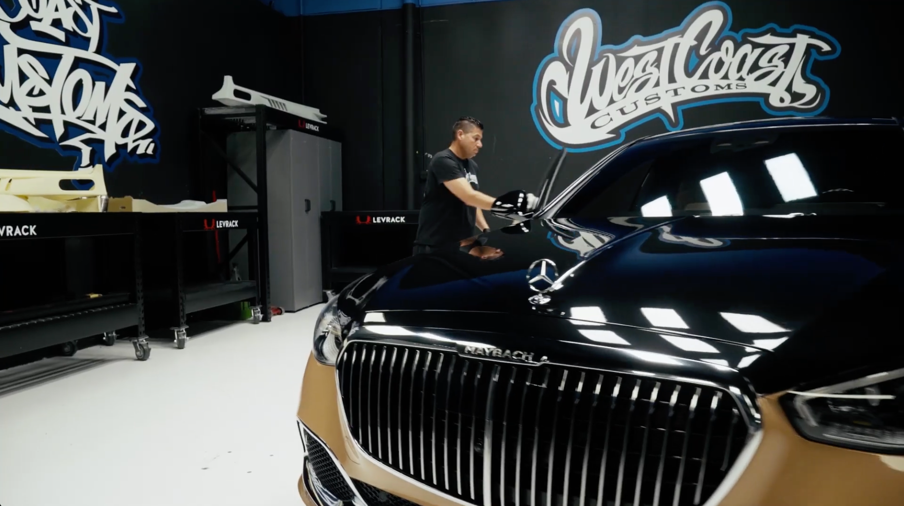 Person working on a black Mercedes-Benz car in a garage with 'West Coast Customs' branding.