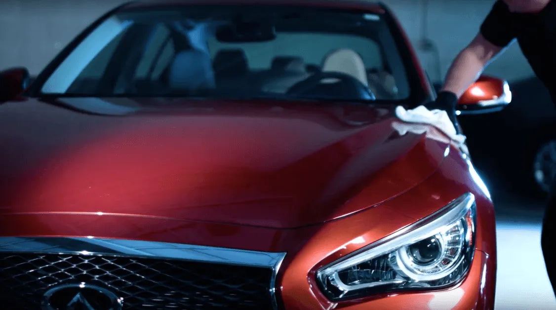 Person cleaning a red Infiniti car with a white cloth.