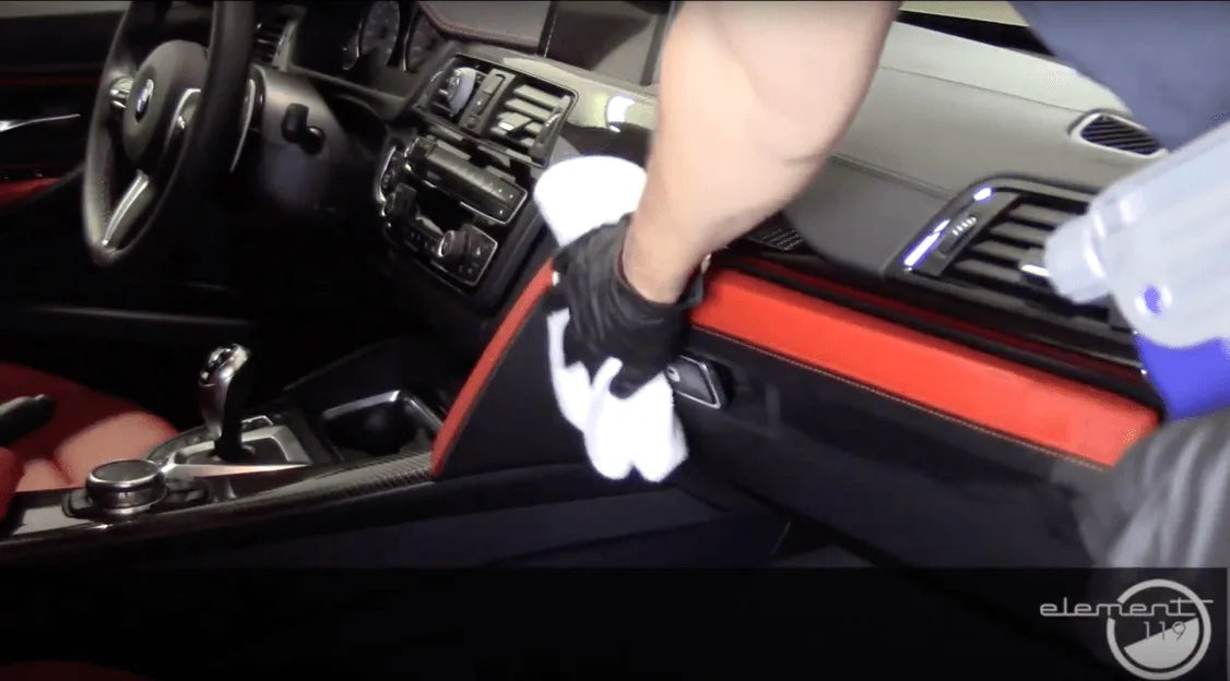 Person cleaning car interior with a cloth and spray bottle, focusing on dashboard.