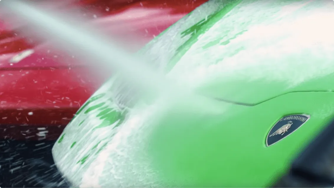 Close-up of a green car being washed with water spraying onto it.